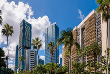 Modern Condos Apartments Against The Giant Clouds In The Blue Sky Background In Miami, Florida. There Are Palm Trees At The Front Of The Multi-storey Residential Buildings With Modern Structures.