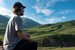 © Chepko Danil - Young man preforms yoga in mountains, Explorer look in summer mountain breathing fresh air, teenager in headphones listening music in nature