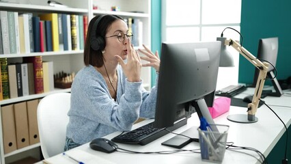 Wall Mural - Young beautiful hispanic woman student sitting on table having video call at library university