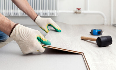 Man in protective gloves lays a laminate on the floor. Repair and decoration of premises. Modern flooring. Soft focus.