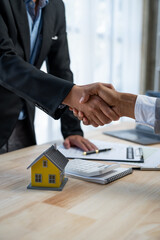 Two young Asian businessmen shake hands after signing a contract to invest in a village project. real estate, with businesswomen joining in showing joy and clapping in the office.