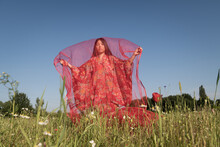 Portrait Of Asian Girl In Red Traditional Kimono Standing In Field Of Poppies Under Thin Fabric