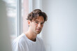 © Westend61 - Smiling young man in front of white wall by window