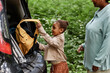 © Seventyfour - Side view portrait of black little girl putting backpack in car trunk while travelling with mom