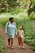 © Seventyfour - Vertical portrait of black mother and daughter walking on nature trail together holding hands