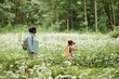 © Seventyfour - Side view portrait of mother and daughter walking across field of forest flowers while hiking together