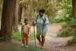 © Seventyfour - Full length portrait of black mother and daughter hiking together walking in beautiful forest trail, copy space