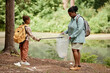 © Seventyfour - Side view portrait of black mother and daughter helping cleaning nature together and picking up trash by river, copy space