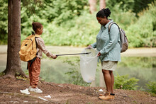 Side View Portrait Of Black Mother And Daughter Helping Cleaning Nature Together And Picking Up Trash By River, Copy Space 