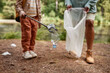 © Seventyfour - Close up of little girl picking up plastic bottle outdoors helping clean nature, copy space