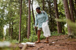 © Seventyfour - Full length portrait of eco activist black woman picking up trash in nature trail, copy space