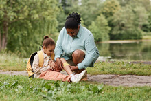 Portrait Of Caring Black Mother Putting Band Aid On Knee Of Little Girl Injured During Nature Hike, Copy Space 
