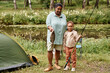 © Seventyfour - Full length portrait of happy mother and daughter fishing together looking at camera during camping in nature