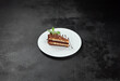 Peanut and caramel cake with chocolate topped on white plate on dark stone background. Piece of Snickers cake in minimal style. Toffee, nuts and chocolate cake in confectionery menu.
