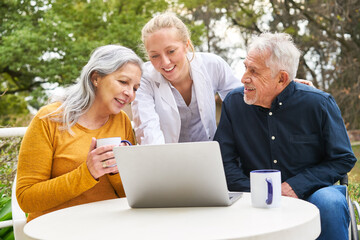 Wall Mural - Doctor explaining elderly couple over laptop at table in garden