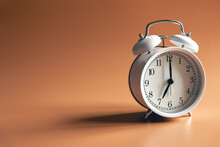 White Alarm Clock On Brown Background Isolated.
