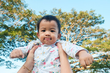 Mom hand lifting happy 1 year baby boy in tree park