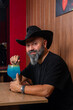© Rafa - hombre barman con gorro de vaquero preparando un cóctel azul en la barra del bar
