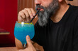 © Rafa - hombre barman con gorro de vaquero preparando un cóctel azul en la barra del bar