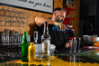 © Rafa - hombre barman con gorro de vaquero preparando un cóctel azul en la barra del bar