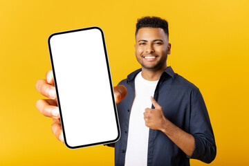 Cheerful Indian man with smartphone in the hand isolated on yellow background, showing smartphone with empty screen and thumbs up, advertising mobile app, showing deal