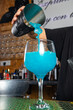 © Rafa - hombre barman con gorro de vaquero preparando un cóctel azul en la barra del bar