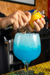 © Rafa - hombre barman con gorro de vaquero preparando un cóctel azul en la barra del bar