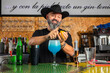 © Rafa - hombre barman con gorro de vaquero preparando un cóctel azul en la barra del bar