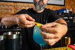 © Rafa - hombre barman con gorro de vaquero preparando un cóctel azul en la barra del bar