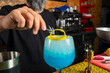 © Rafa - hombre barman con gorro de vaquero preparando un cóctel azul en la barra del bar