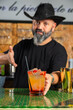 © Rafa - hombre barman con gorro de vaquero preparando un cóctel azul en la barra del bar