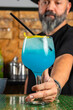 © Rafa - hombre barman con gorro de vaquero preparando un cóctel azul en la barra del bar
