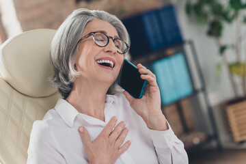 Sticker - Portrait of excited overjoyed aged person sit chair chatting telephone hand chest laughing workplace indoors