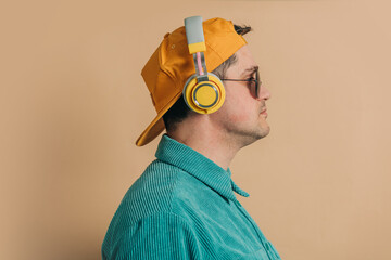 Wall Mural - Stylish caucasian man in green shirt, headphones, sunglasses and cap on brown background