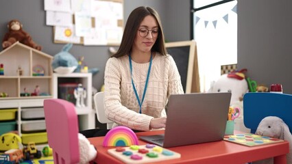 Sticker - Young beautiful hispanic woman preschool teacher using laptop sitting on table at kindergarten