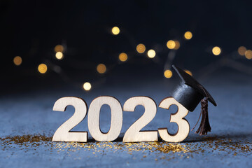 Class of 2023 concept. Wooden number 2023 with graduate hat on dark background with bokeh