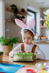 Wall Mural - Happy girl looking at growing plants after decorating easter eggs.