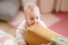 Cute Baby Toddler Bites The Yellow Sofa. Beautiful Portrait Of A Child With Blue Eyes