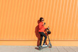 © VISTA by Westend61 - Woman using smart phone with electric push scooter in front of orange wall