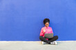 © VISTA by Westend61 - Woman waving on video call through laptop sitting in front of blue wall