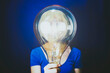 © VISTA by Westend61 - Woman holding large illuminated bulb against blue background