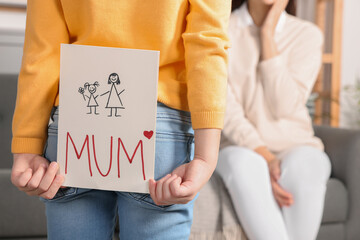 Wall Mural - Little girl hiding greeting card for her mother behind back at home