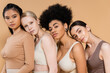 © LIGHTFIELD STUDIOS - young multiethnic women in underwear leaning on each other and looking at camera isolated on beige.
