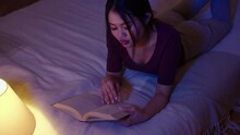 Young beautiful woman reading book while lying in bed at night.
