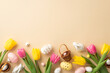 canvas print picture - Easter celebration concept. Top view photo of colorful easter eggs small baskets ceramic bunnies yellow and pink tulips on isolated pastel beige background with copyspace
