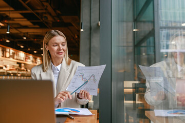 Wall Mural - Businesswoman making online videoconference and demonstrate financial graphs to colleagues in cafe