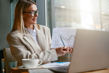 Wall Mural - Businesswoman making online videoconference and demonstrate financial graphs to colleagues in cafe