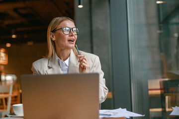 Wall Mural - Attractive businesswoman freelancer working on laptop while sitting in cafe near window