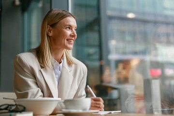 Wall Mural - Smiling businesswoman having lunch and making notes while working in cafe