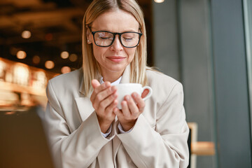 Wall Mural - Attractive businesswoman holding cup of coffee while sitting in cafe during working day
